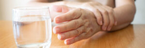 Elderly woman with Parkinson's Disease struggles while reaching for a glass of water on the table