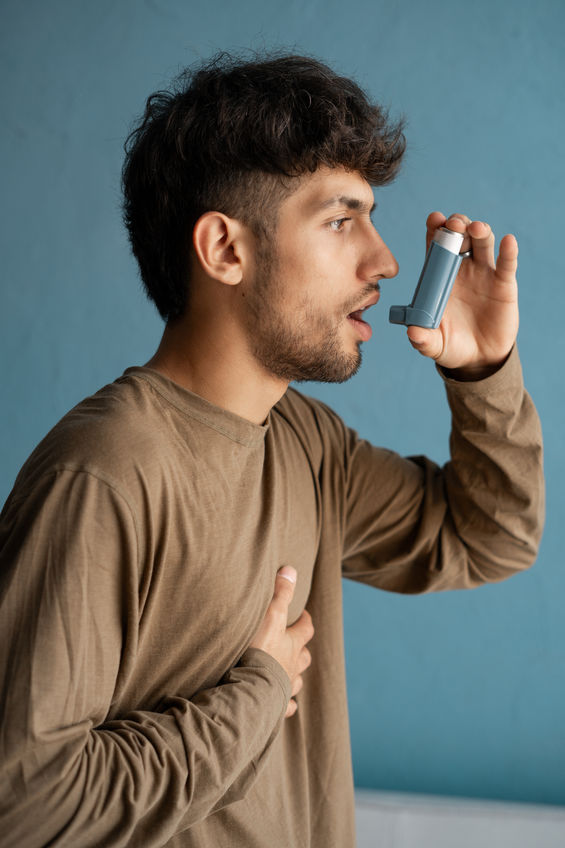 Young man with asthma having difficulty breathing while taking a puff of his inhaler