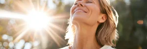 A fibromaylgia patient with pain relief smiles joyfully while looking up at the sun, basking in its warm light.