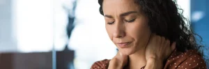 A woman gently holds her neck with both hands, dealing with the pain from fibromyalgia.